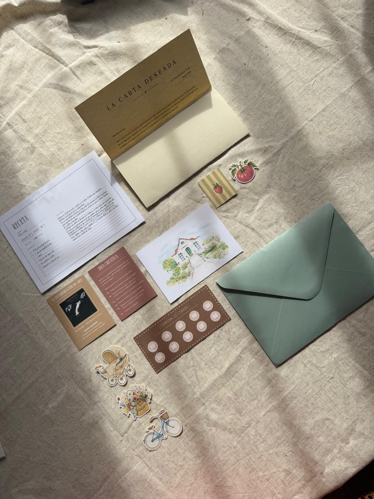 Contenido de La carta deseada sobre una tela: carta, receta, ilustración, pegatinas y un sobre verde.
